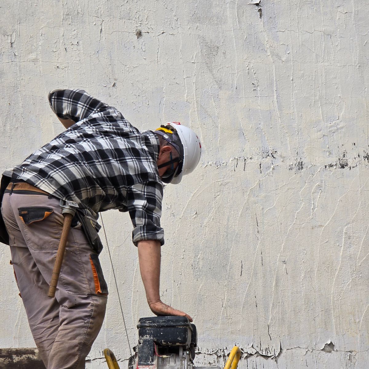 Ouvrier du bâtiment casqué utilisant une machine contre un mur, savoir-faire d'un artisan certifié