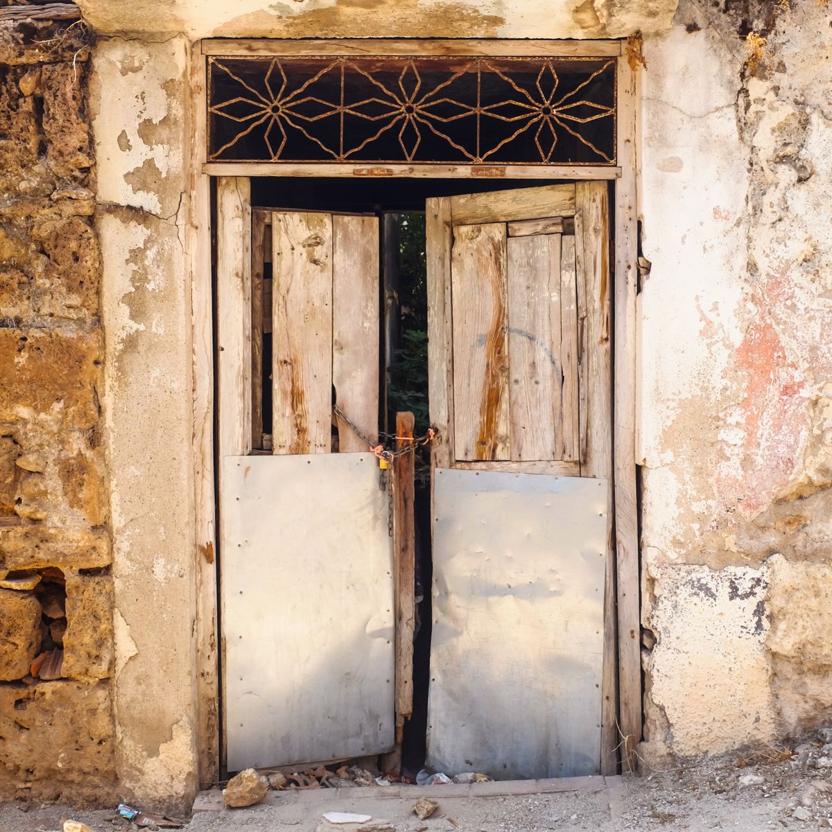 Porte en bois massif avec ferrures métalliques éclairée par le soleil, détail du battant