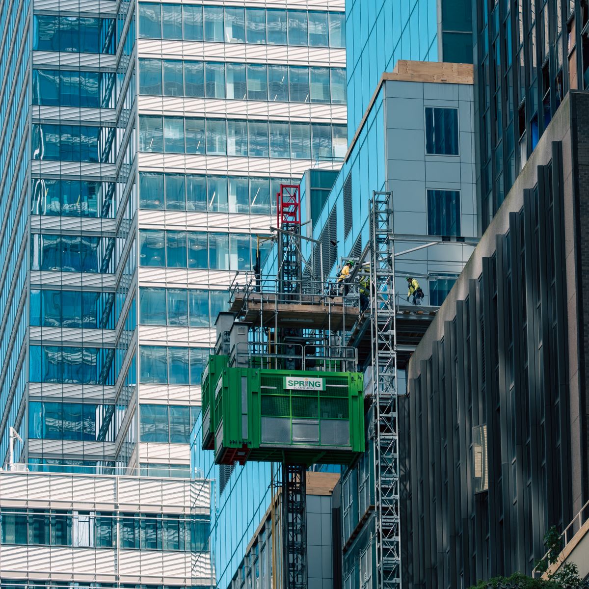 Ouvriers du bâtiment sur un chantier urbain avec monte-charge devant des immeubles vitrés