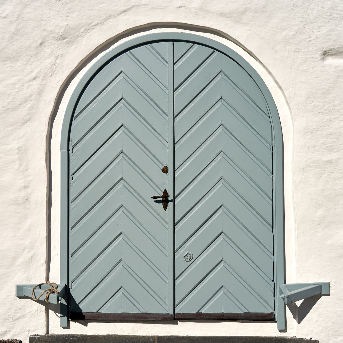 Porte d'entrée en bois cintrée à motifs chevrons bleu-gris intégrée à une façade